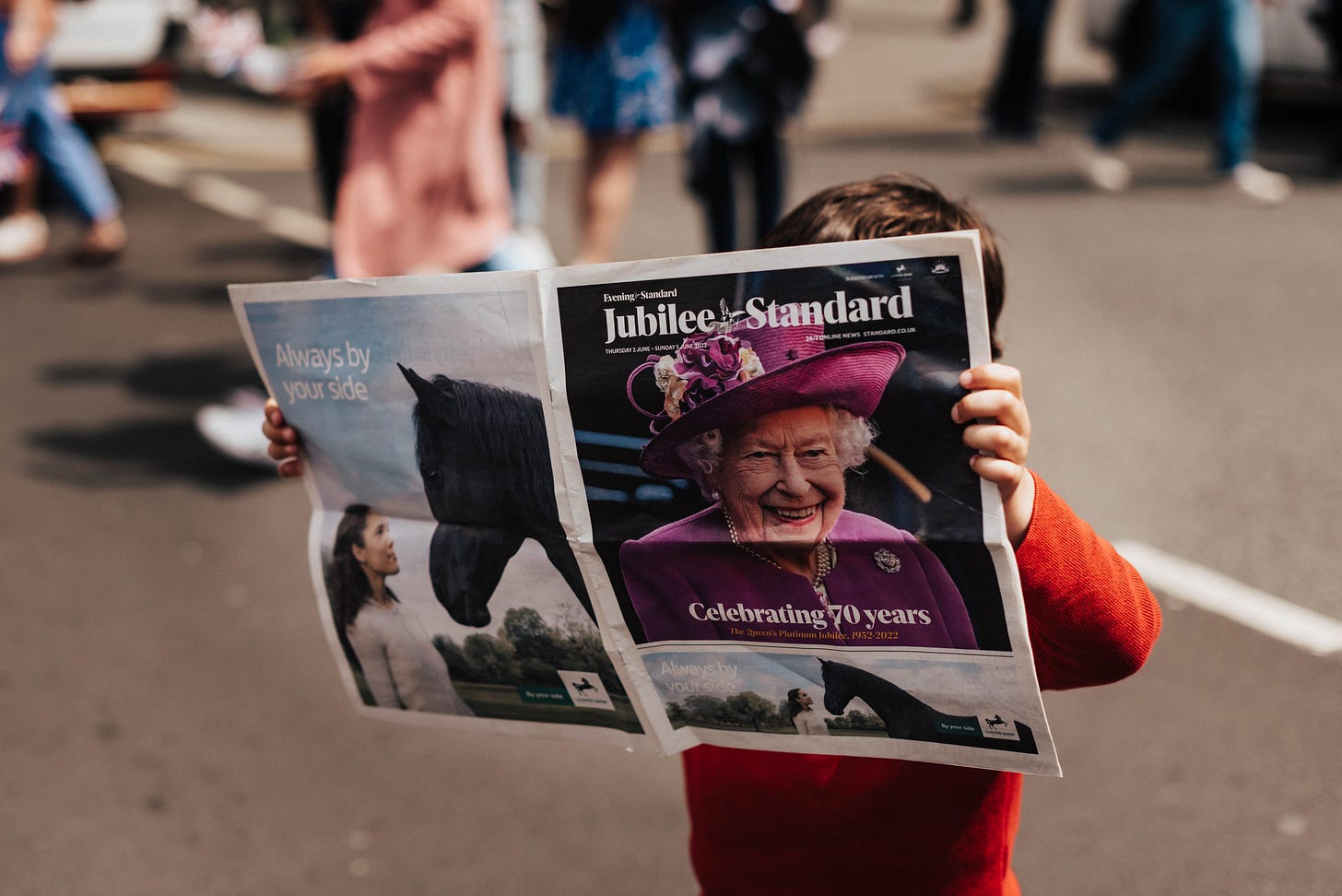 Small boy holding newspaper with picture of Queen Elizabeth II on front page