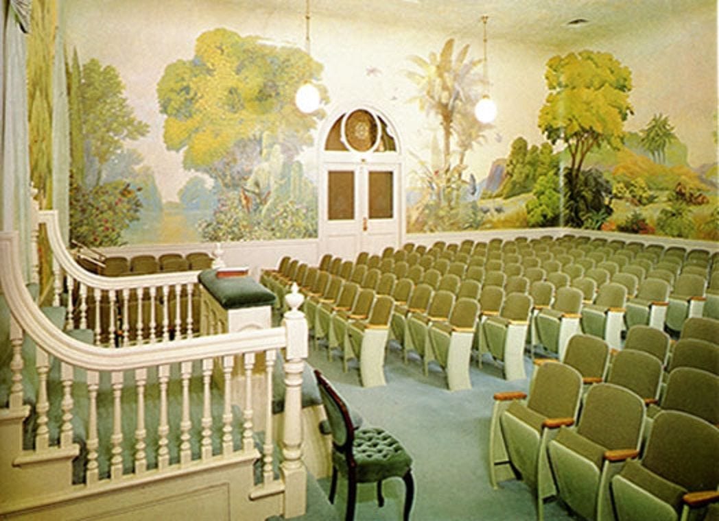 SLC Temple Garden of Eden murals with trees and lush landscapes. There are rows of chairs and a white staircase with a curved banister.