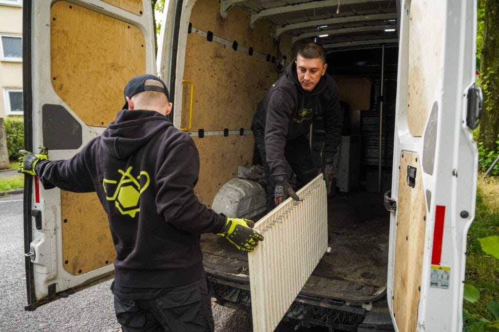The picture shows two SchrottBienen employees picking up a radiator.