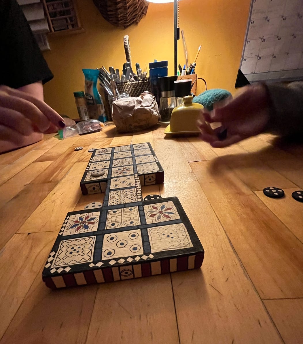 A funny shaped board game sits on the table. It is a long painted board with many squares painted in different patterns