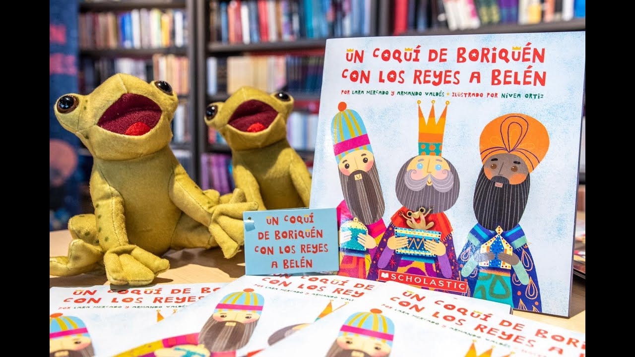 Copies of the book "Un Coquí de Boriquén con los Reyas A Belen" sit on a table with two stuffed coqui.