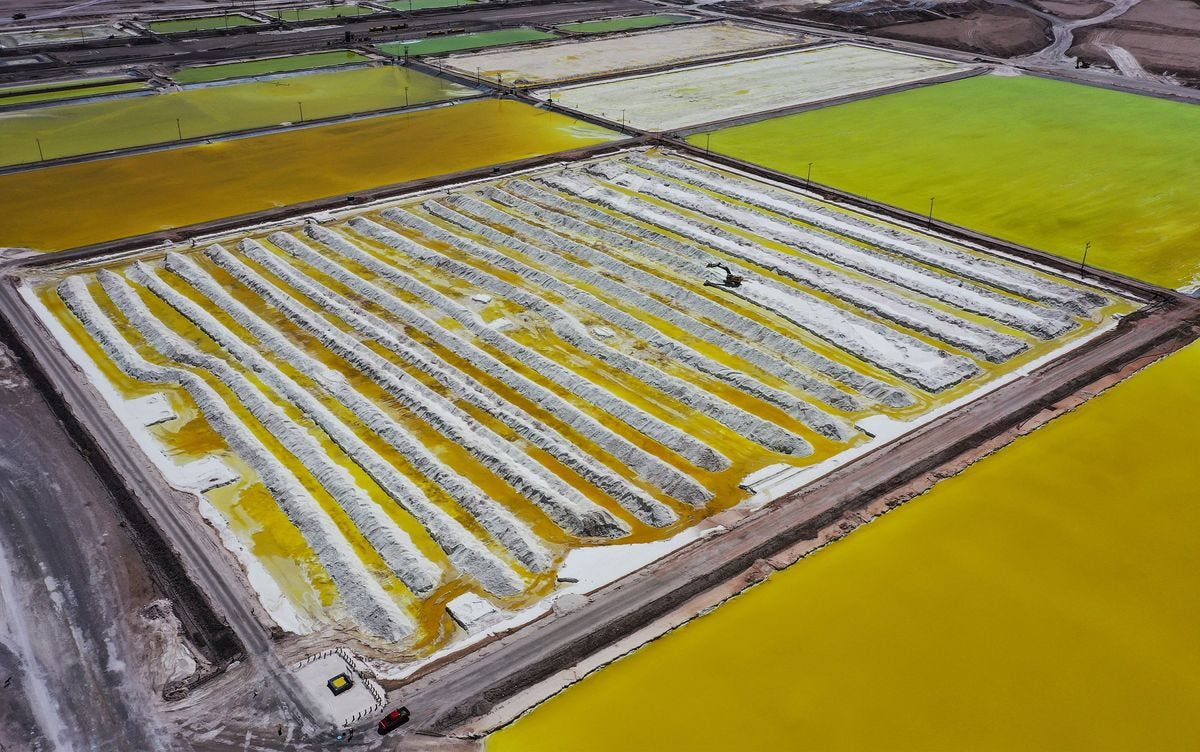 Aerial photo of large ponds of green and yellow, one of which has rows of large white mounds, and a piece of heavy machinery.