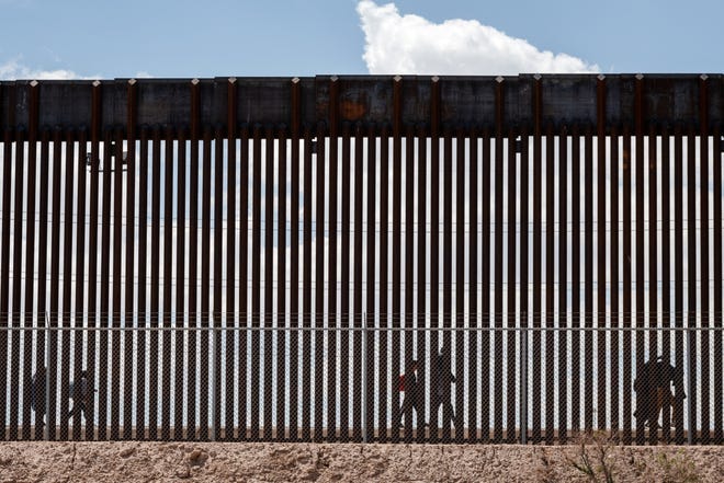 Migrants walk along the Mexico-U.S. border wall in El Paso, Texas on March 19, 2024.