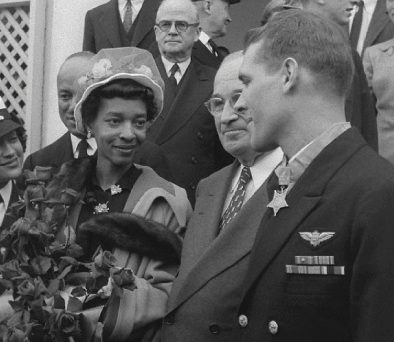 Thomas Hudner receives his Medal of Honor as Jesse Brown's widow looks on.  She is smiling at Hudner.