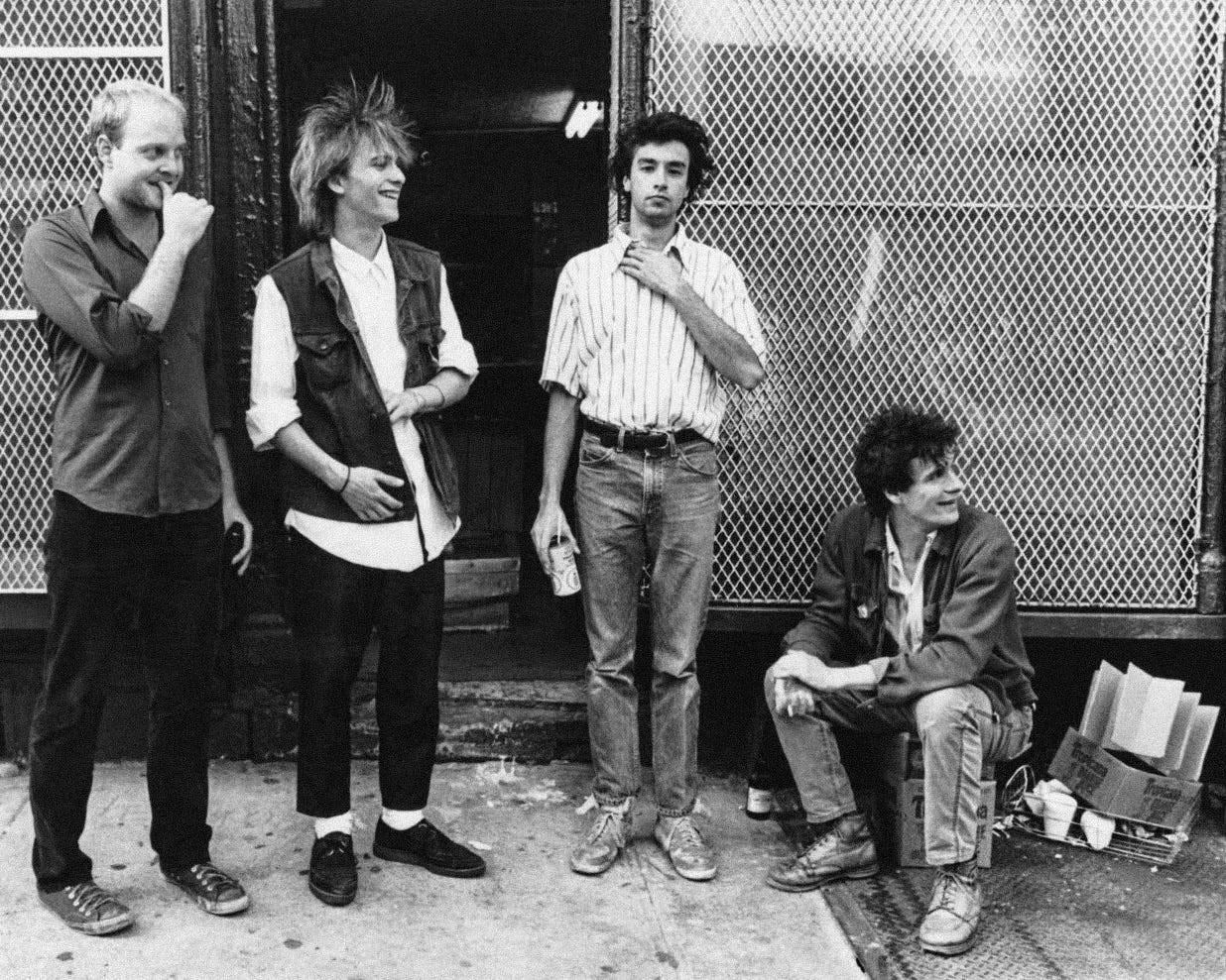 The members of the Replacements in front of a chain link fence.