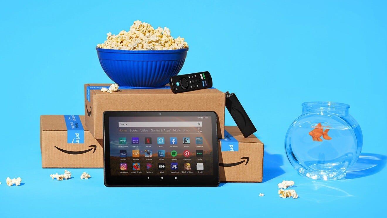 An image of a bucket of popcorn sitting atop stacked Amazon boxes. In front of the boxes is a tablet and there is a goldfish in a bowl next to all of it.