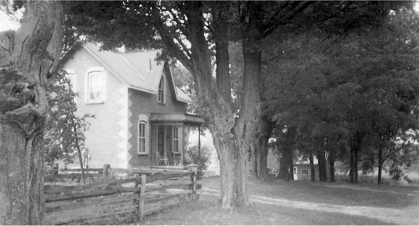 Black and white photo of an attractive 2-story brick house with a small awning over the front door and large trees all around. The snug house appears to have about 800 square feet per floor.