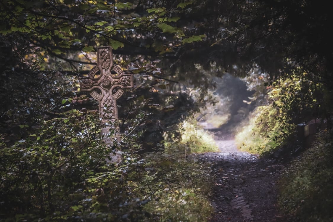 Free Ornately Carved Celtic Stone Cross on a Side of a Forest Trail Stock Photo