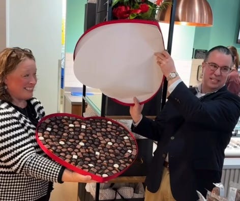 A person and person holding a heart shaped box of chocolate

Description automatically generated