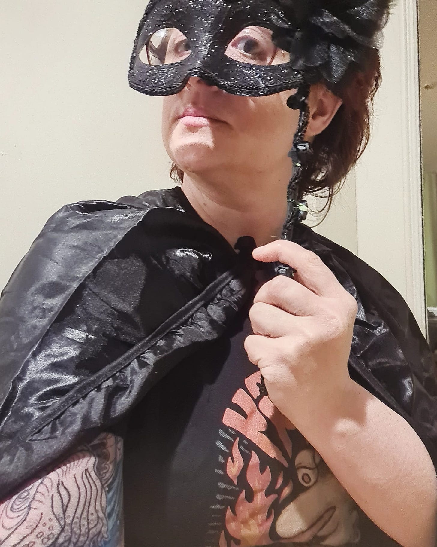 A woman wearing a black mask and cape, attempting to look villainous