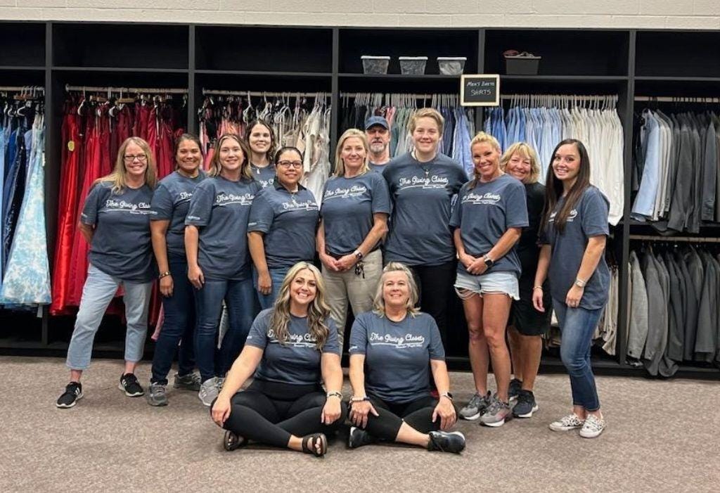 Happy, proud group of people standing in front of racks of neatly organized clothing at Ann E's Closet.