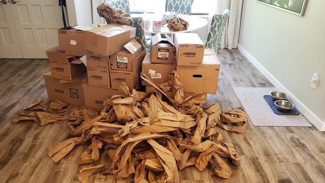 A stack of more than a dozen cardboard boxes and a pile of packing paper sit in the front room of a nicely appointed house. 