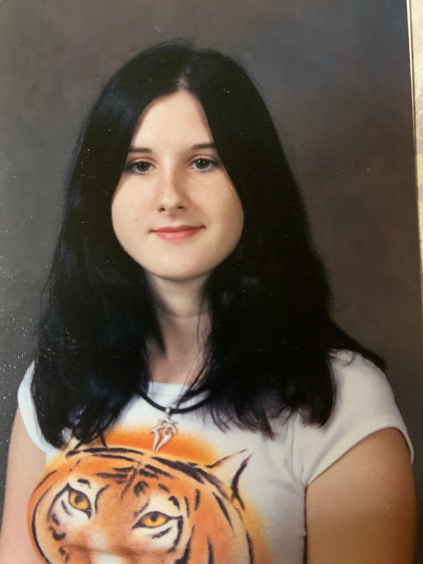 Lyric (then Kat) in high school, posing for a school photo with long dark hair.