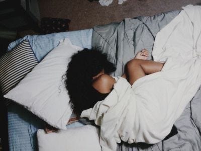This may contain: a woman laying on top of a bed covered in white sheets and pillows with her head under the covers