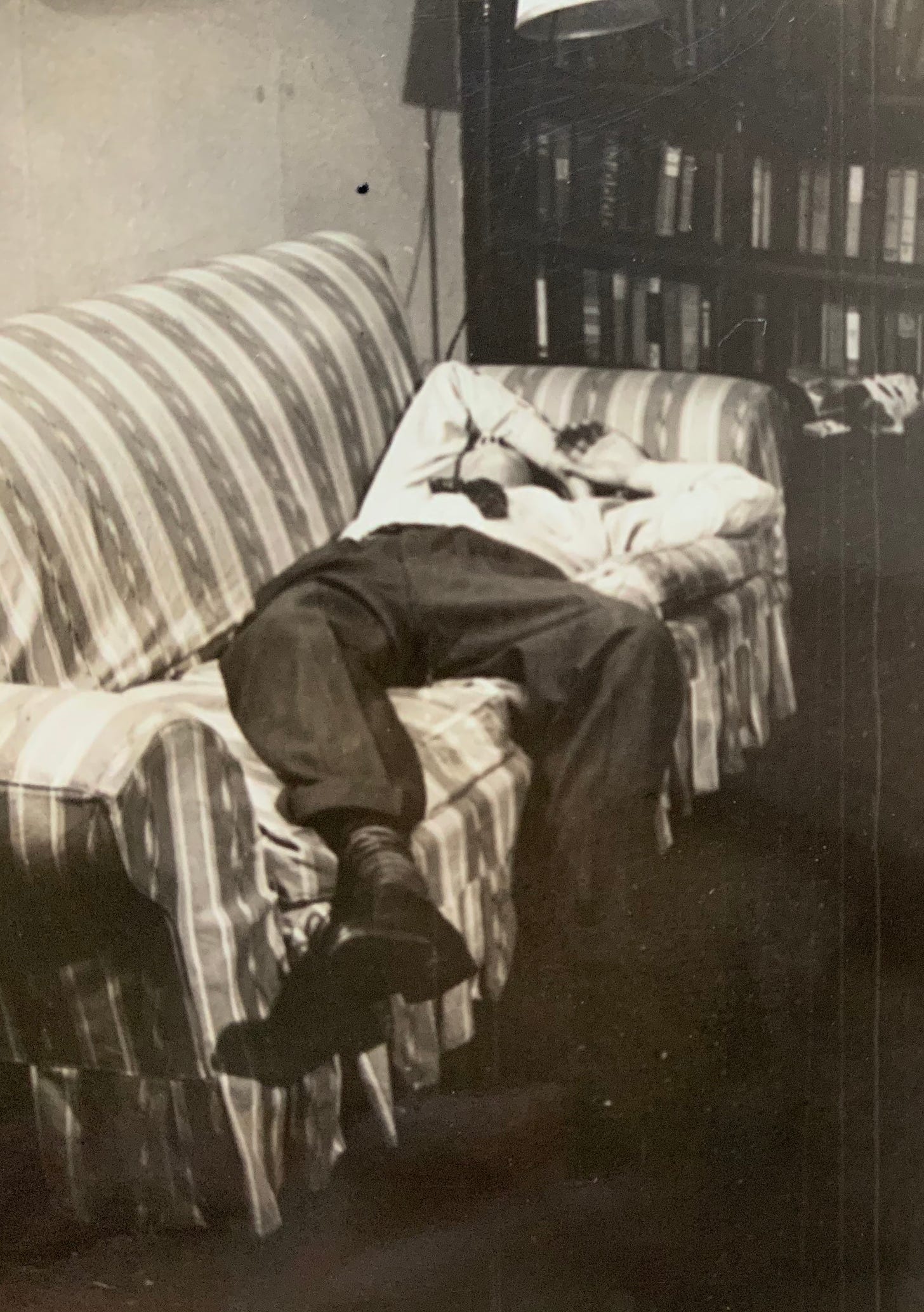 a vintage black and white snapshot of a man lying on a couch with his arm over his eyes