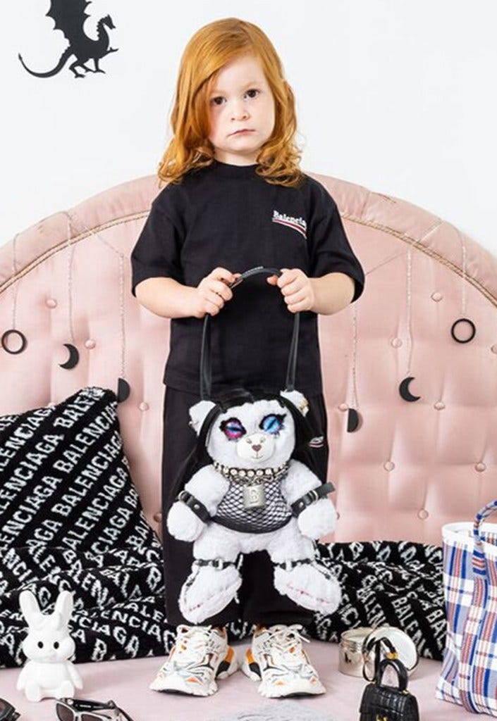 A young girl is pictured holding a teddy bear in bondage style gear on the gift shop section of the Balenciaga website.
