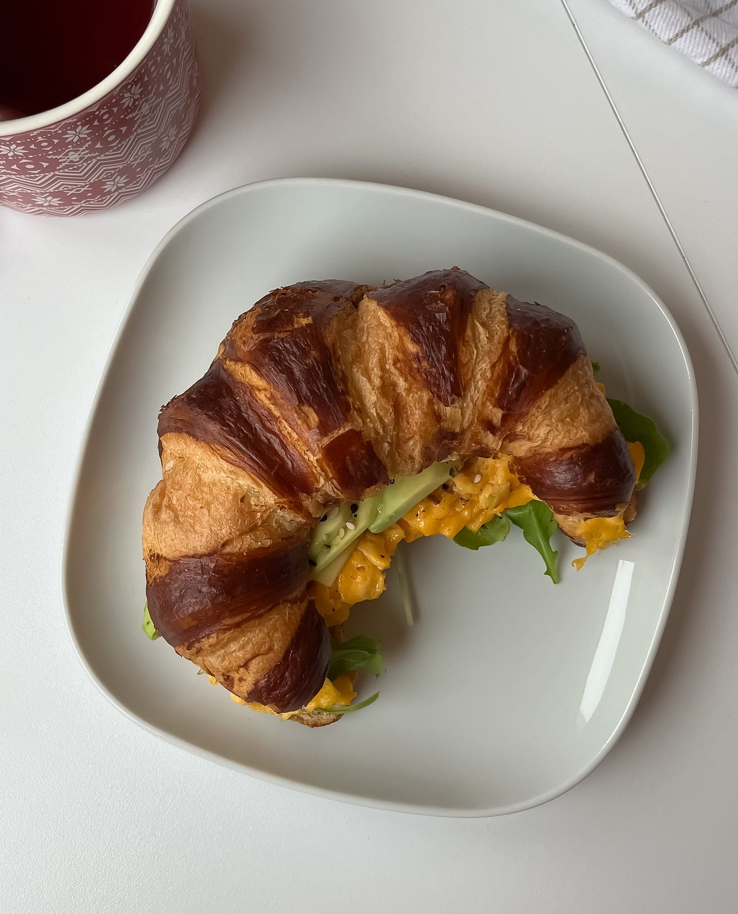 Pretzel croissant breakfast sandwich with eggs, melted cheese, avocado, and a sprinkle of everything bagel seasoning.
