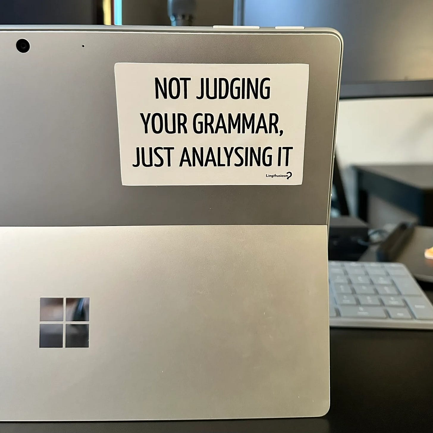 A sticker on a laptop that says “Not judging your grammar, just analyzing it,” made by Lingthusiasm.