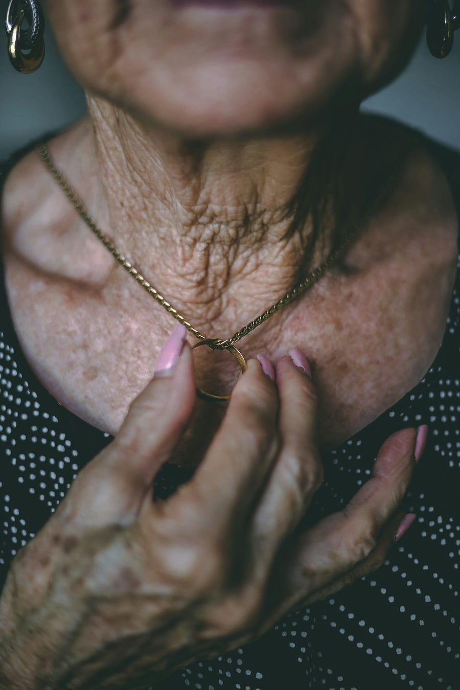 An elderly person holds a locket on a chain around her neck. An elderly person holds a locket on a chain around her neck.