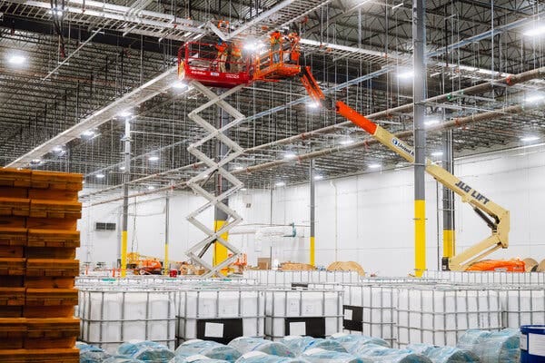 Two construction cranes inside a large brightly lit warehouse.