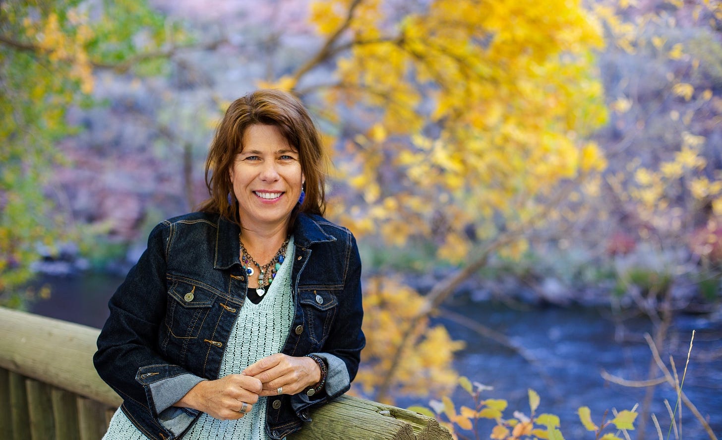 laura pritchett leaning against a bridge, fall colored trees in background