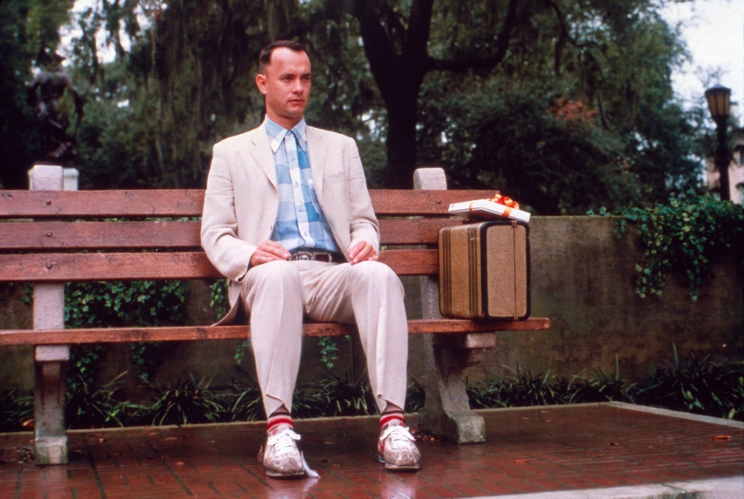 Film still from the opening scene of the movie Forrest Gump, Tom Hanks sits on a bench, box of chocolates and his suitcase on his left