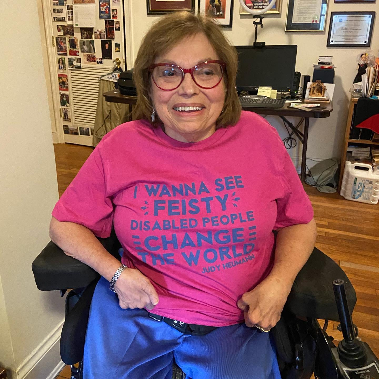 Judy wearing a pink shirt that reads her quote "I wanna see feisty disabled people change the world."