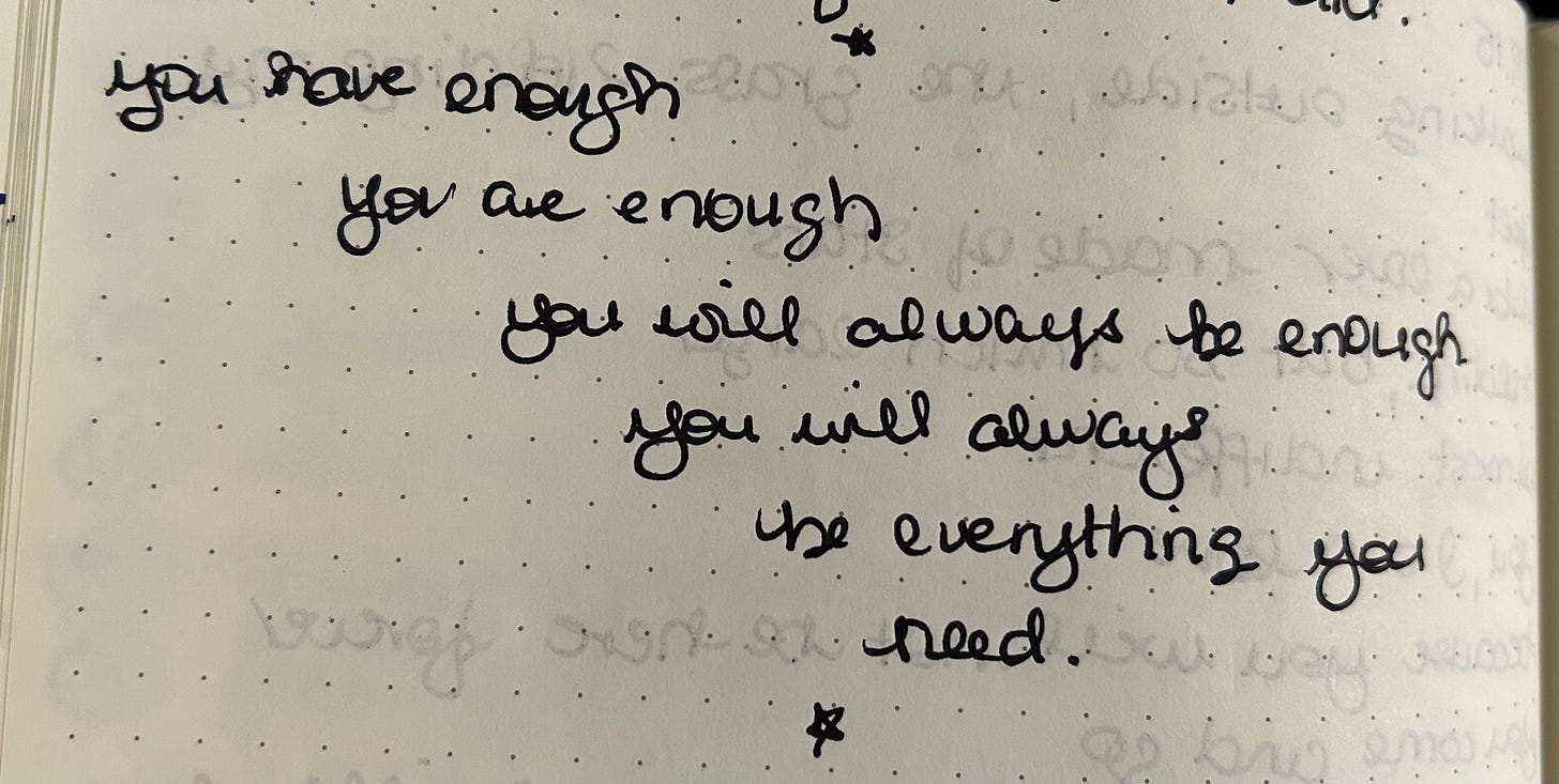 Black cursive writing on a white page. The poem says: you have enough / you are enough / you will always be enough / you will always / be everything you need.