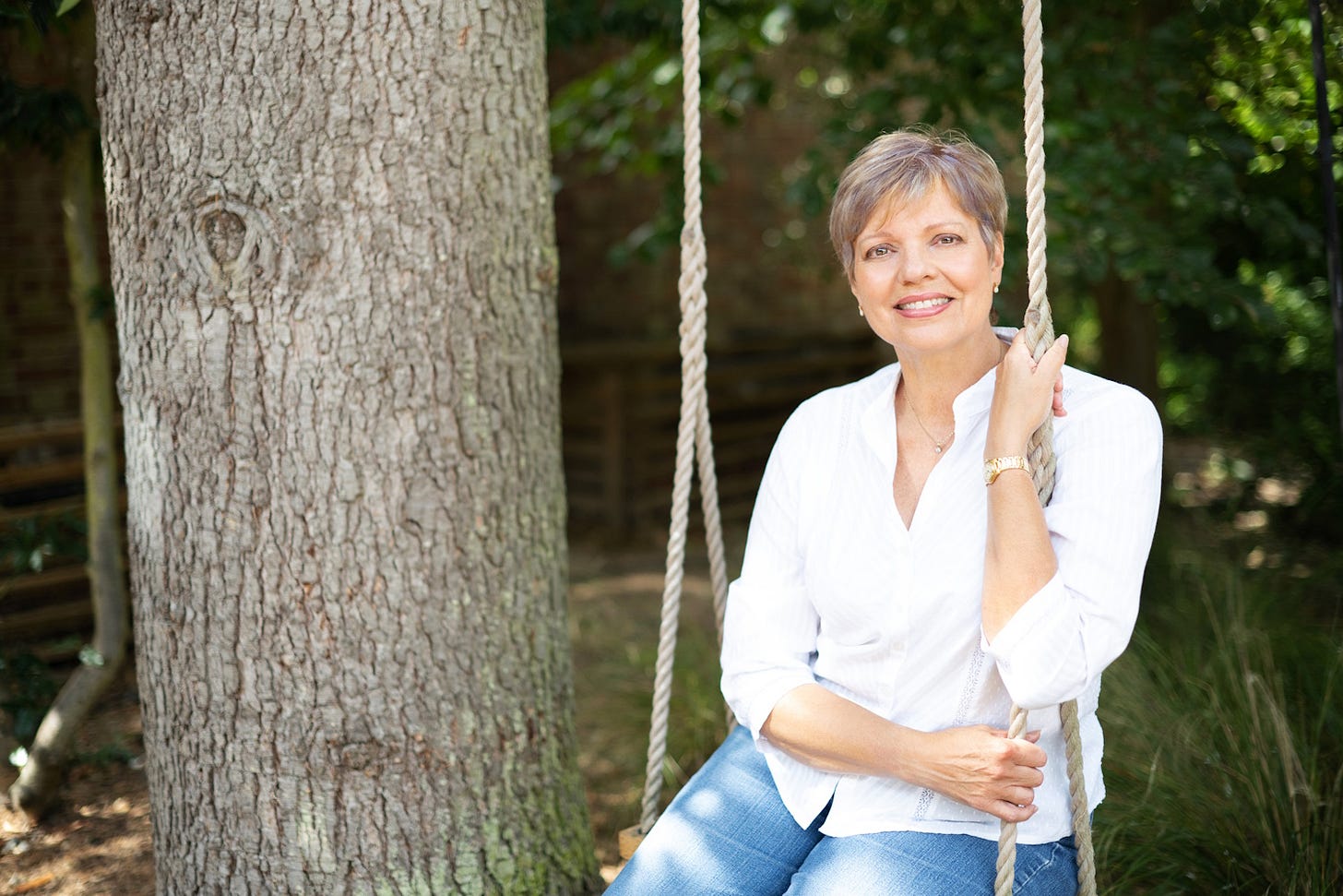 Smiling mid-life woman, wearing a white shirt and jeans, sitting on a tree swing