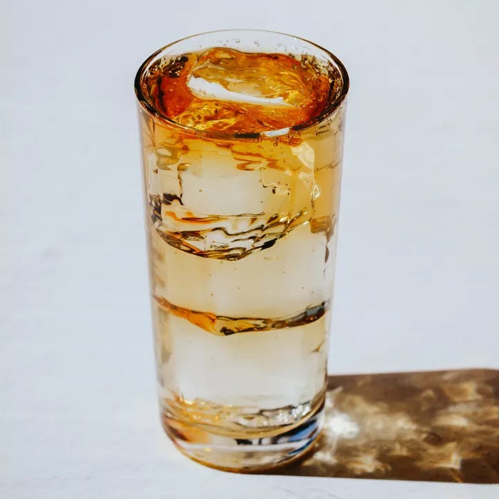 A Collins glass filled with clear ice cubes and an amber-hued effervescent drink