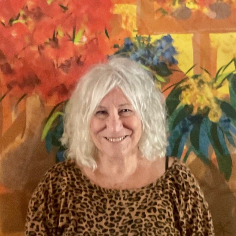 Portrait of Artist Sherry Killam in front of a large floral with orange, gold, and greens.