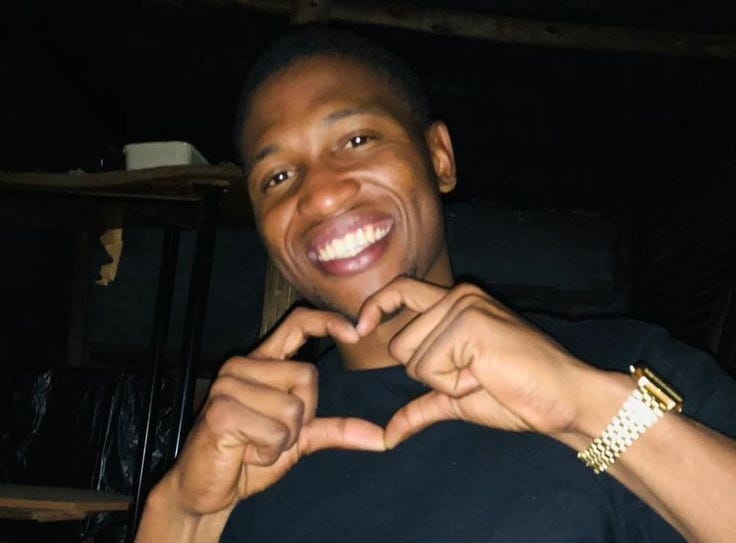 This may contain: a young man making a heart with his hands while sitting in front of a table