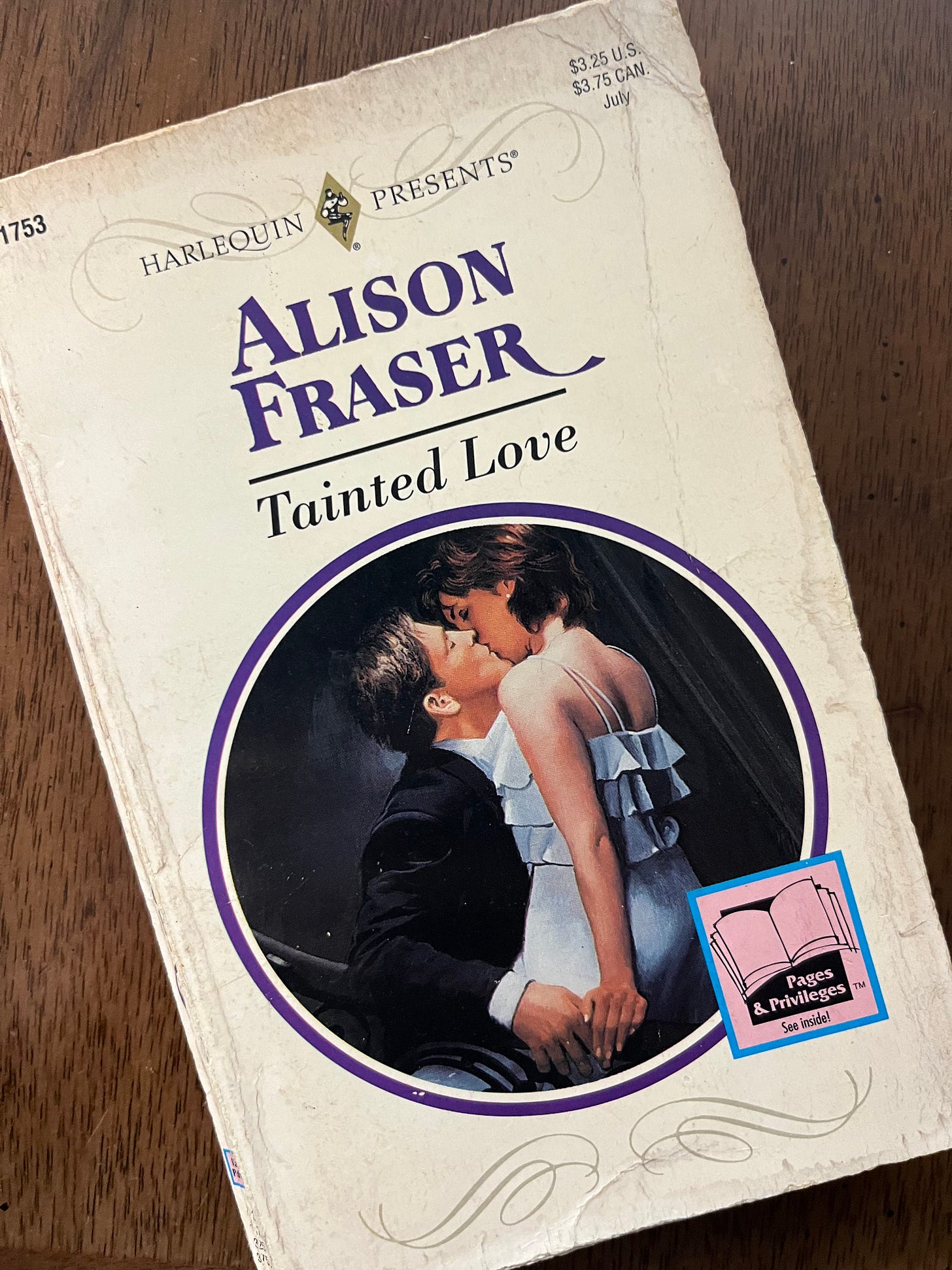Image of front cover of Tainted Love, which shows a very realistic illustration of a man in a tux sitting and a woman kinda in his lap, maybe sitting on the arm of the chair, they're kissing passionately, she's wearing a ruffled dress, their hands are touching