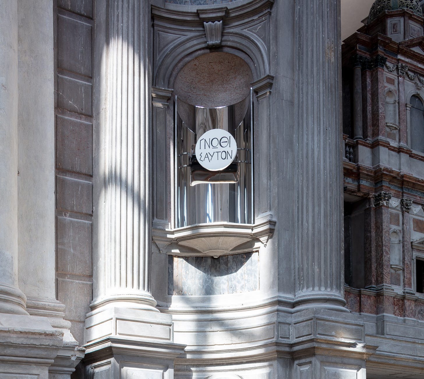 A mirror object set into an altar niche reads Greek text.