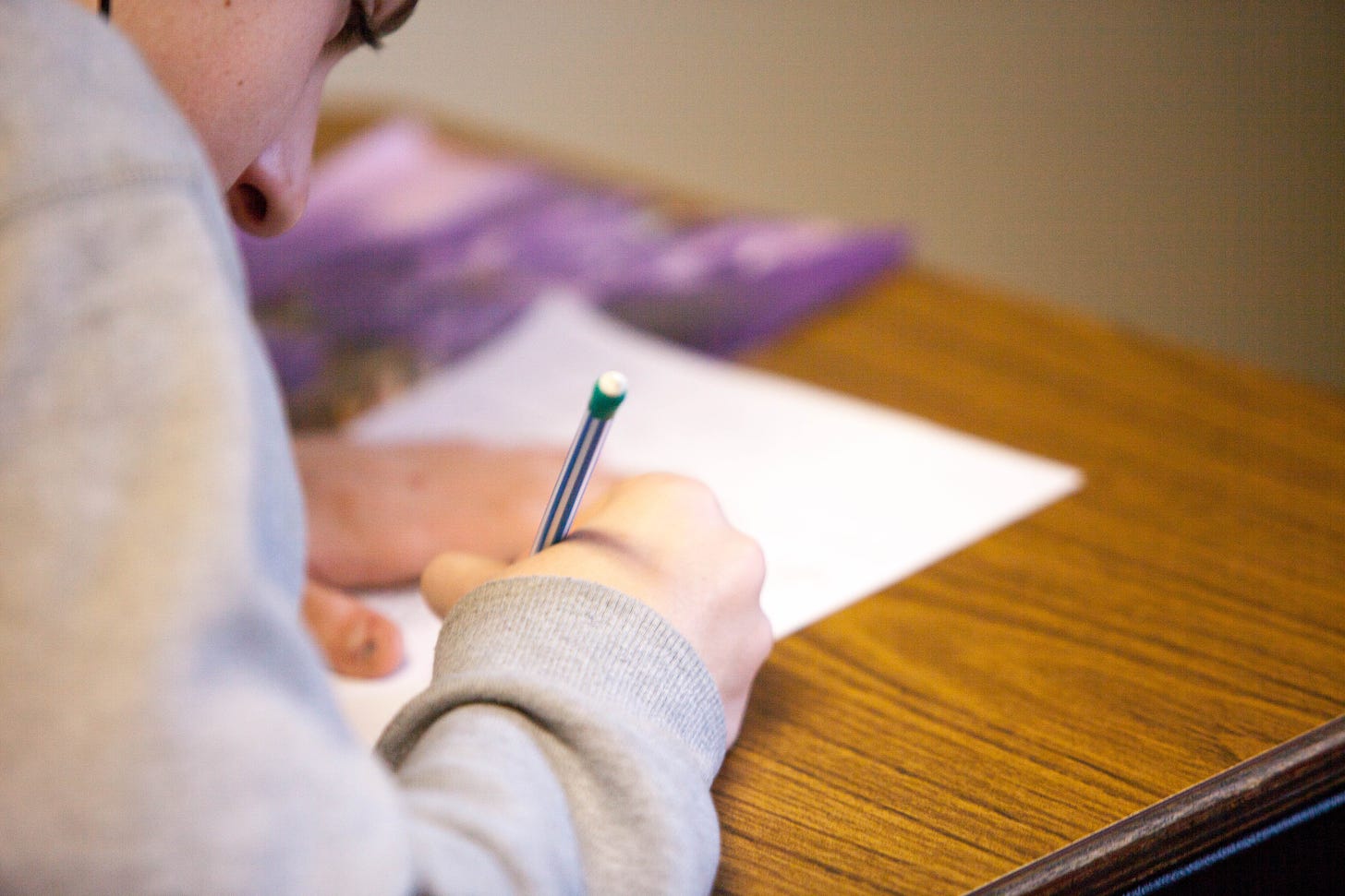 Close up photo of a person leaning over a desk writing with a pencil on a piece of paper