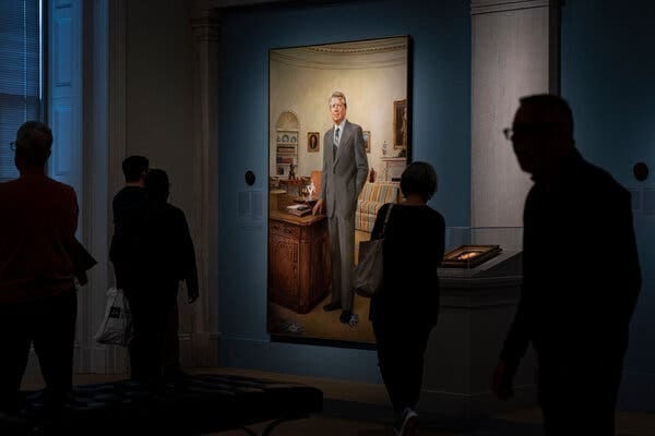 Dark silhouettes of people walking through a museum. Illuminated in the middle is a tall portrait of Mr. Carter during his presidency.