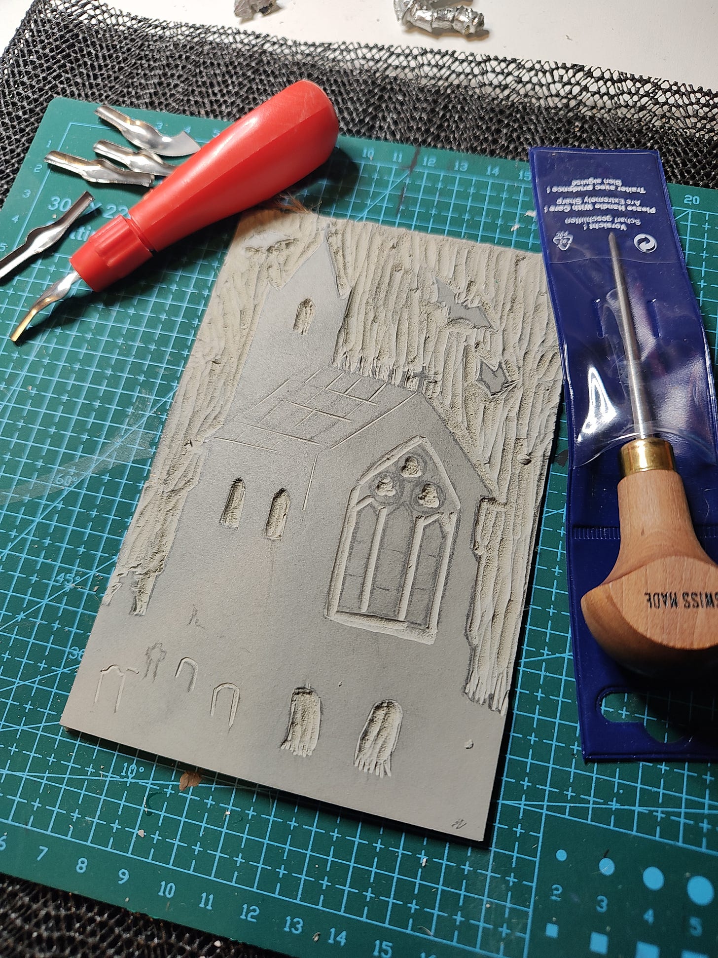 Photo of a carved piece of lino depicting a church surrounded by bats, accompanied by various lino cutting tools
