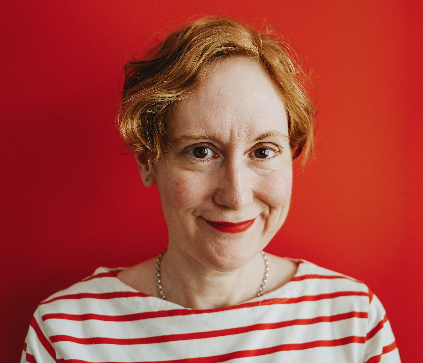 Woman with red hair wearing a striped shirt against a red background