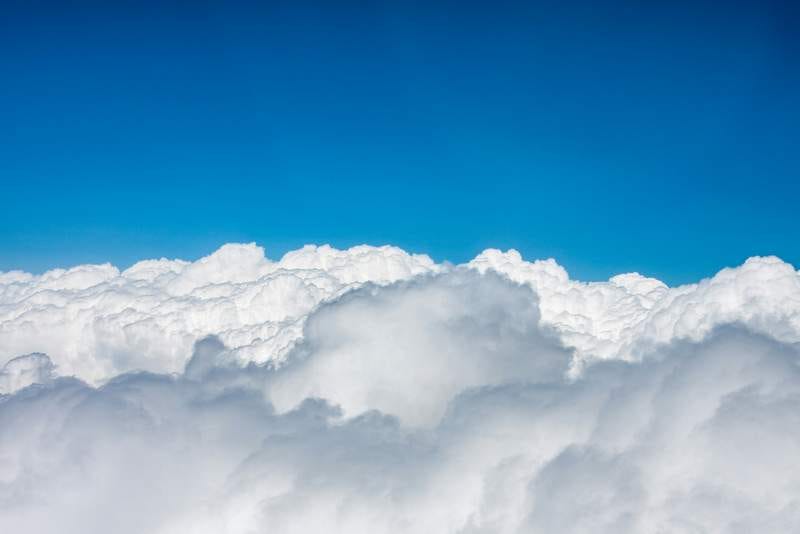 Photo looking down on thicky, fluffy grey-white clouds under a clear blue sky.