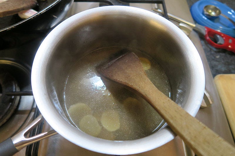 A saucepan on a stovetop full of chicken stock and slices of ginger.