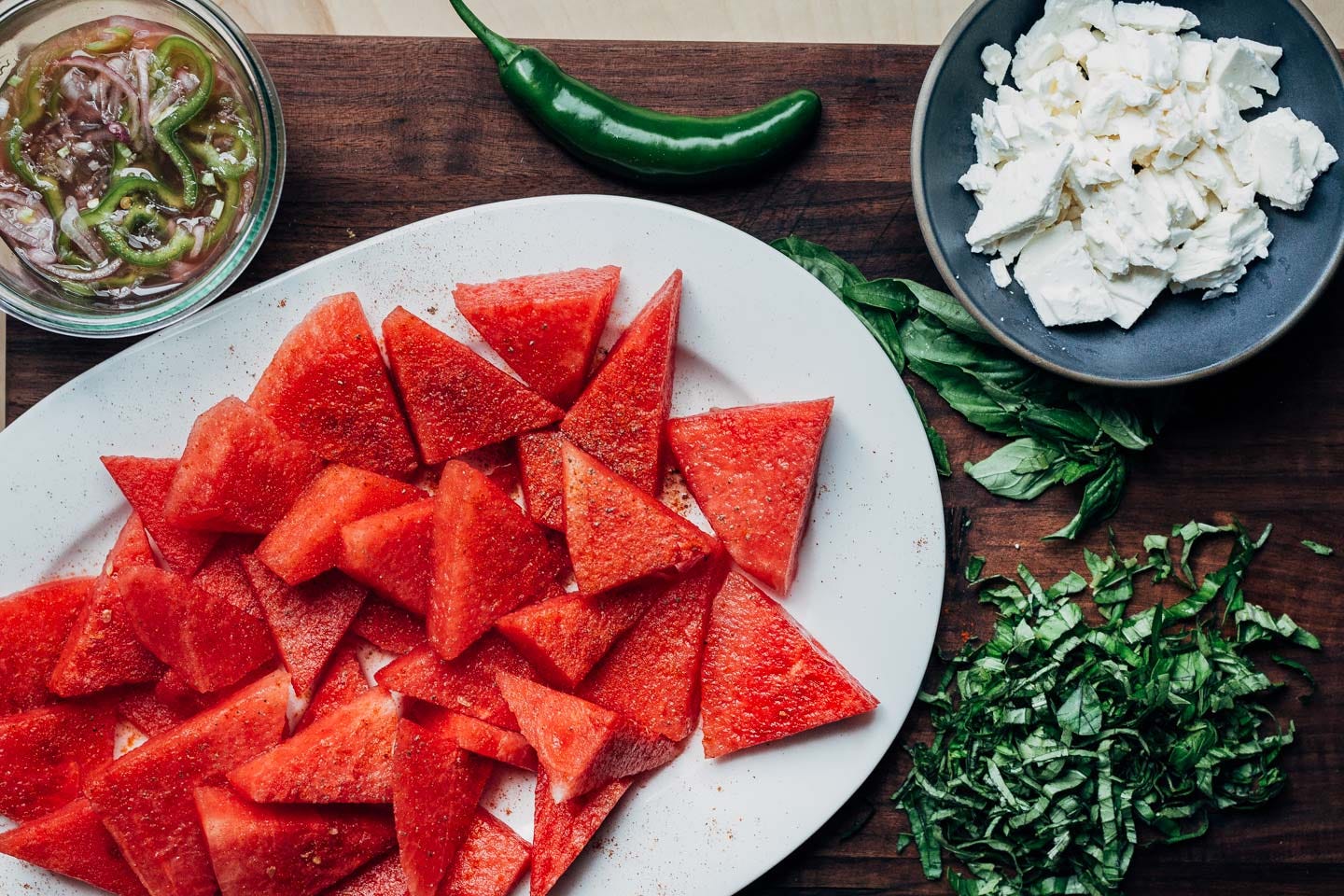 Ingredients for a watermelon salad arranged on a cutting board. 