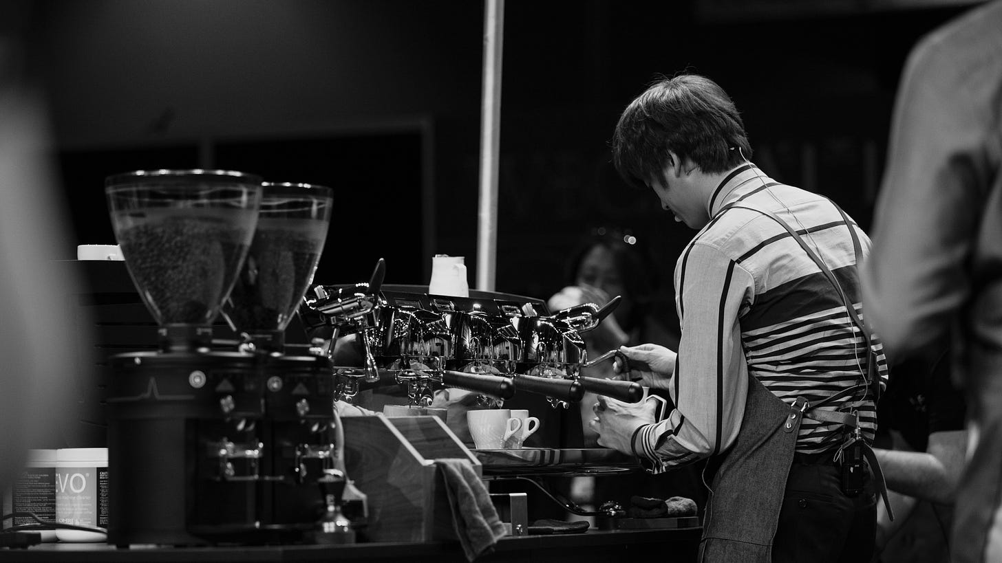 A barista competitor with their back to the camera steams milk on an espresso machine at the World Barista Championship