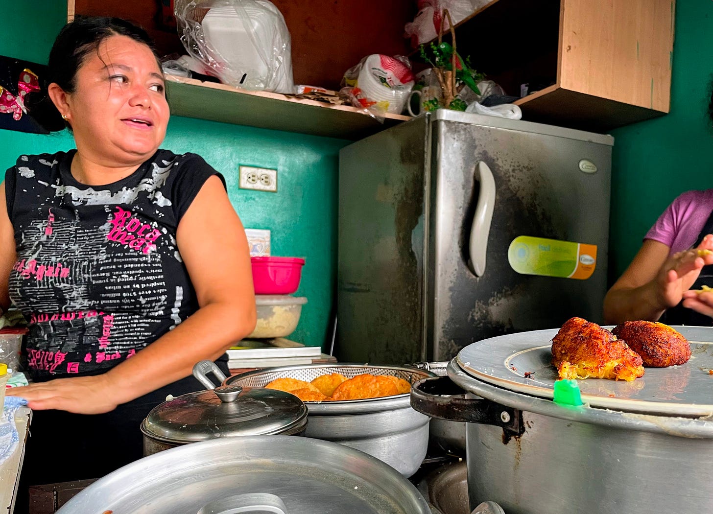 A woman laughs while making street food in a small kitchen