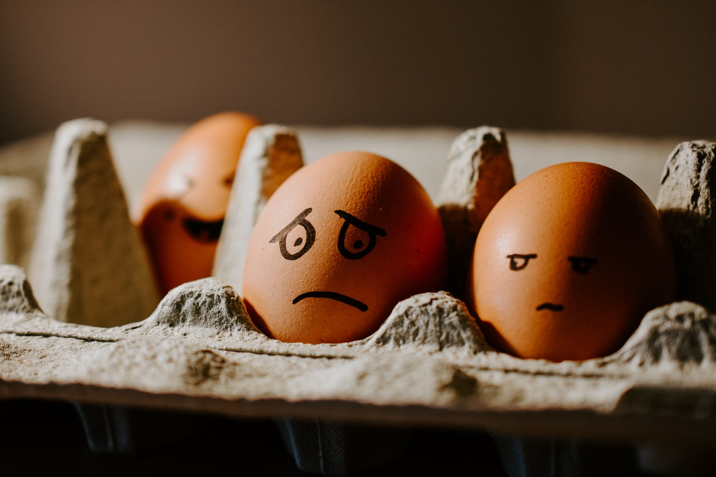 3 brown eggs in a carton with different faces drawn on: happy, worried, side-eye