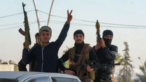 Getty Images Três jovens segurando armas posam na traseira de uma caminhonete. Um tem um RPG, outro está segurando uma metralhadora pesada. O homem na frente segura um rifle de assalto estilo AK47 e está levantando os dedos em saudação.