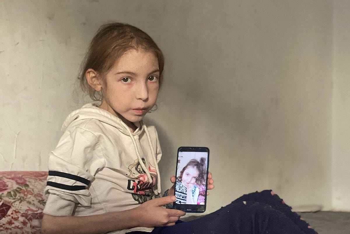 Twelve-year-old Rahaf Ayad holds a phone showing a picture of herself before the war, in her family's home in Gaza City, May 2, 2025. (Ahmed Ahmed)