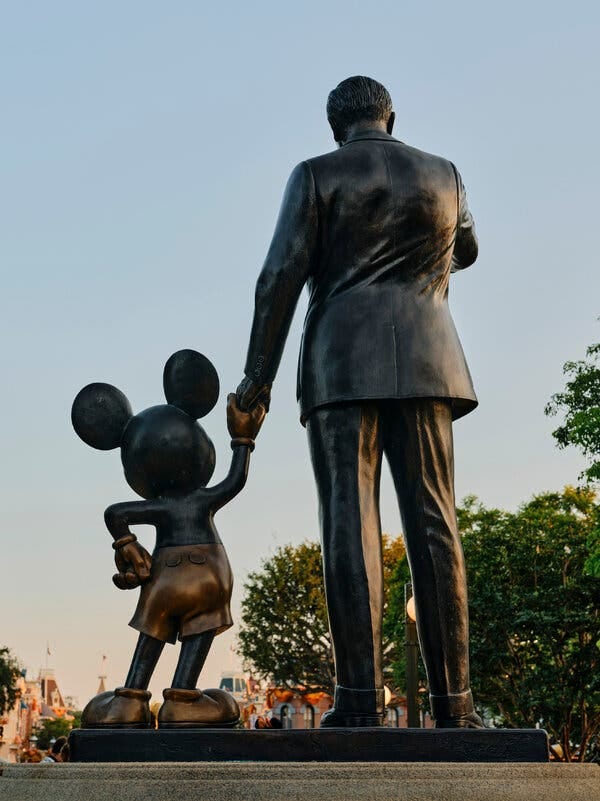 A statue of Mickey Mouse holding the hand of Walt Disney, seen from behind. 