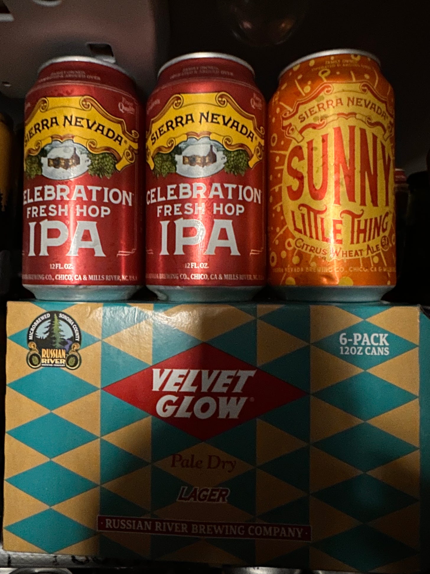 two cans of Celebration Ale next to a can of Sierra Nevada Sunny Little Thing on top of a six pack of Velvet Glow cans from Russian River