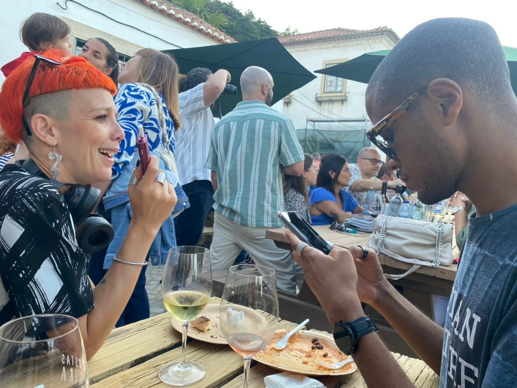 Two cool people - with a lady with orange hair on the left - sat at a table outdoors