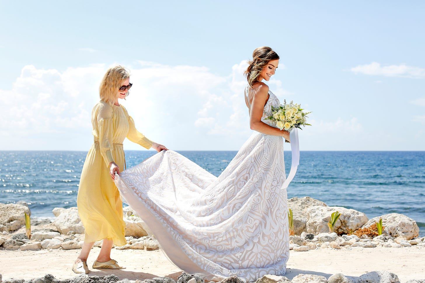 A wedding planner helps a bride with her dress. Two women by the sea at a wedding